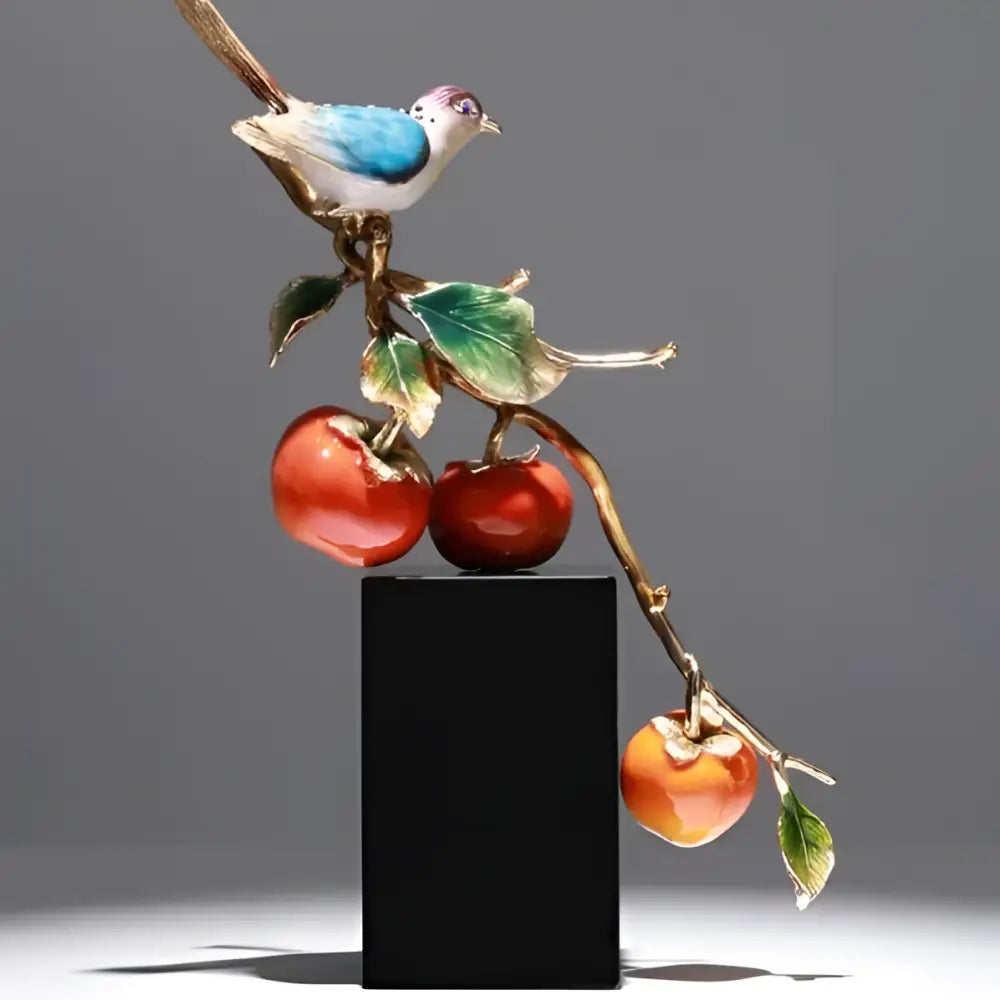 A delicate porcelain bird perched on a golden branch with vibrant red enamel persimmon ruyi and green leaves decor