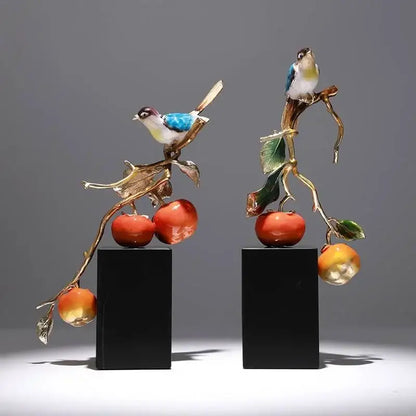 Two enamel persimmon ruyi ornaments featuring blue and white birds on golden branches with red persimmons on black bases
