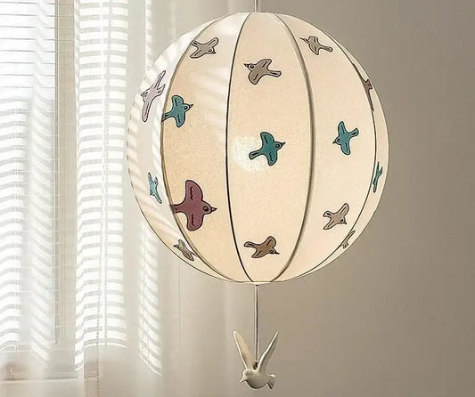 A cream-colored spherical paper pendant light with colorful bird illustrations and a white bird ornament decorbites chinese medieval dove