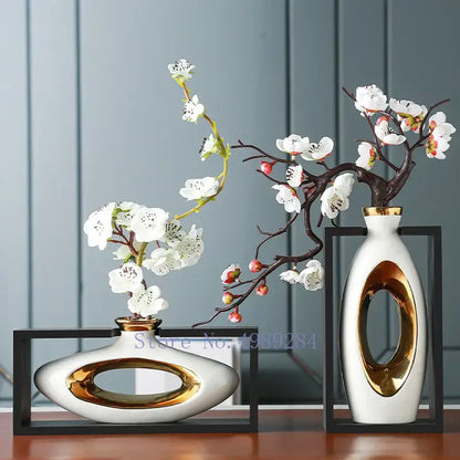 Two modern ceramic vases with gold accents holding white blossoms in a decorbites chinese style ceramic wooden frame