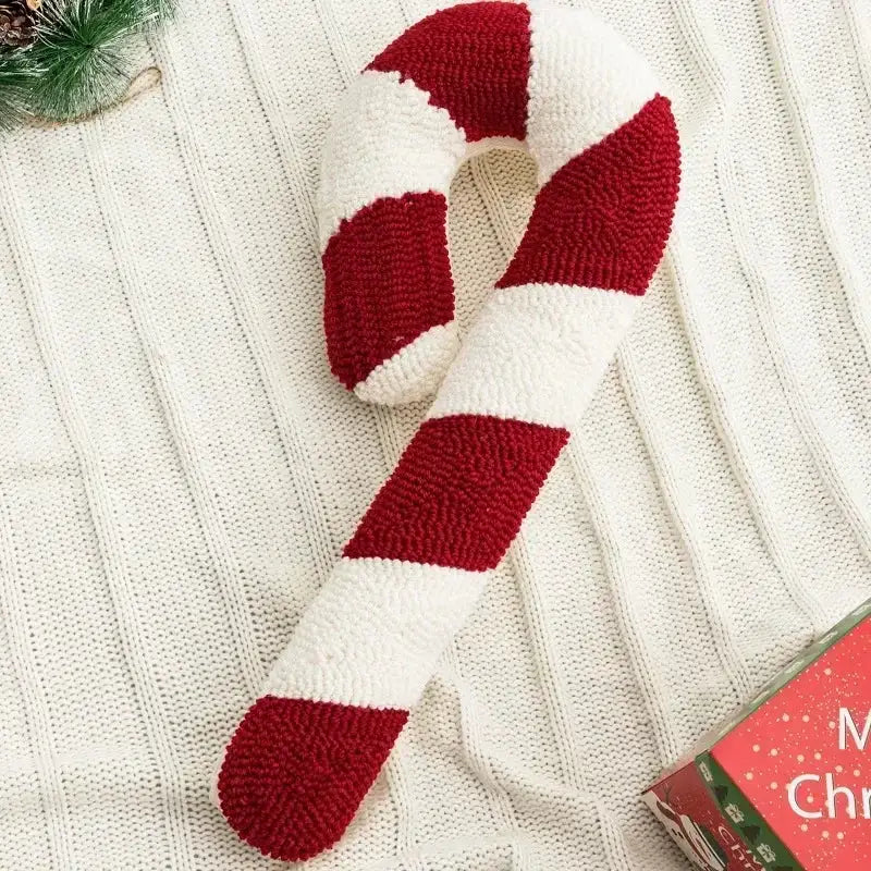 A cozy hand-knitted decorbites christmas candy cushion shaped like a candy cane in bold red and white stripes