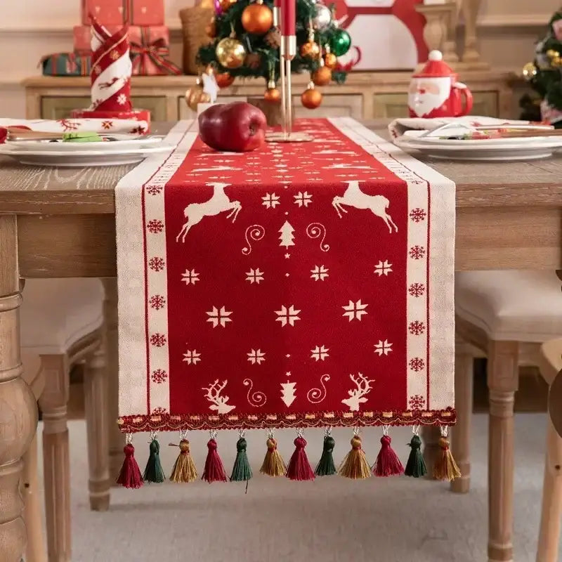 Red christmas table runner with white reindeer and snowflakes, cream border, and colorful embroidered tassel for dining room decor