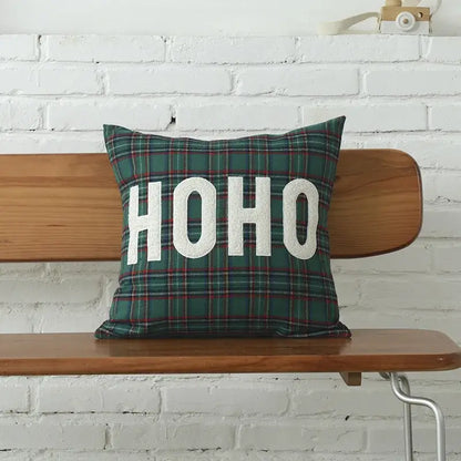 A festive green christmas plaid cotton cushion cover with bold white ho ho lettering by decorbites on a wooden bench