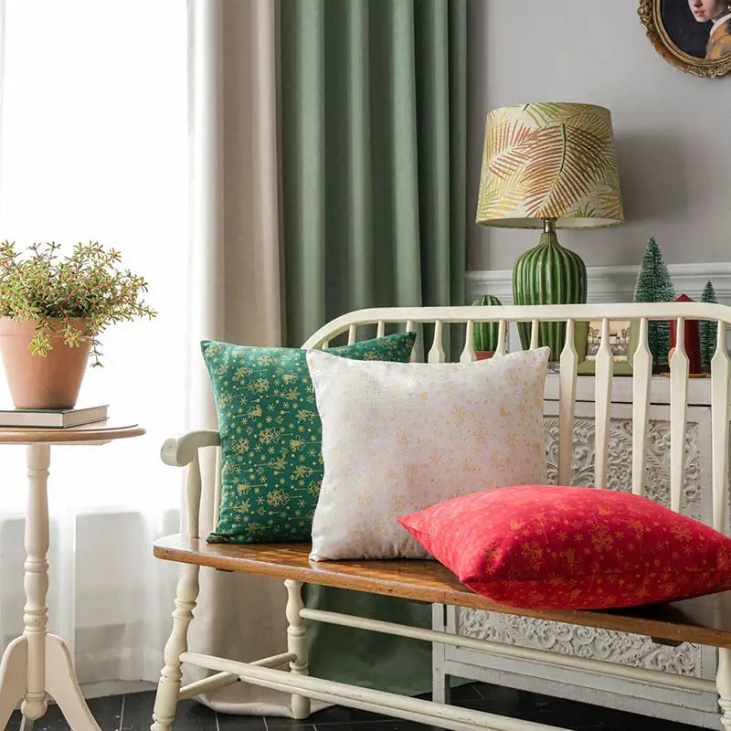 Three decorative decorbites christmas plaid cushion covers in green cream and red with floral patterns on wooden bench