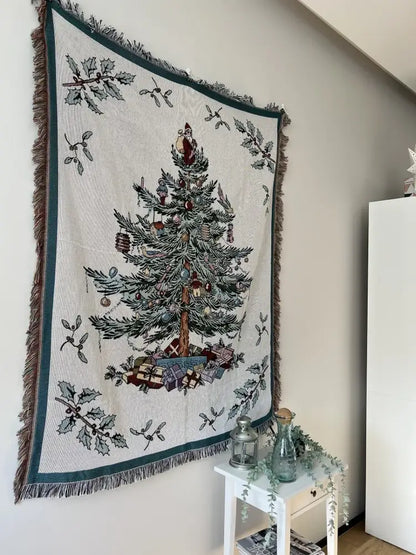 Cream-colored decorbites christmas throw blanket with woven christmas tree design framed by dark green borders and fringes