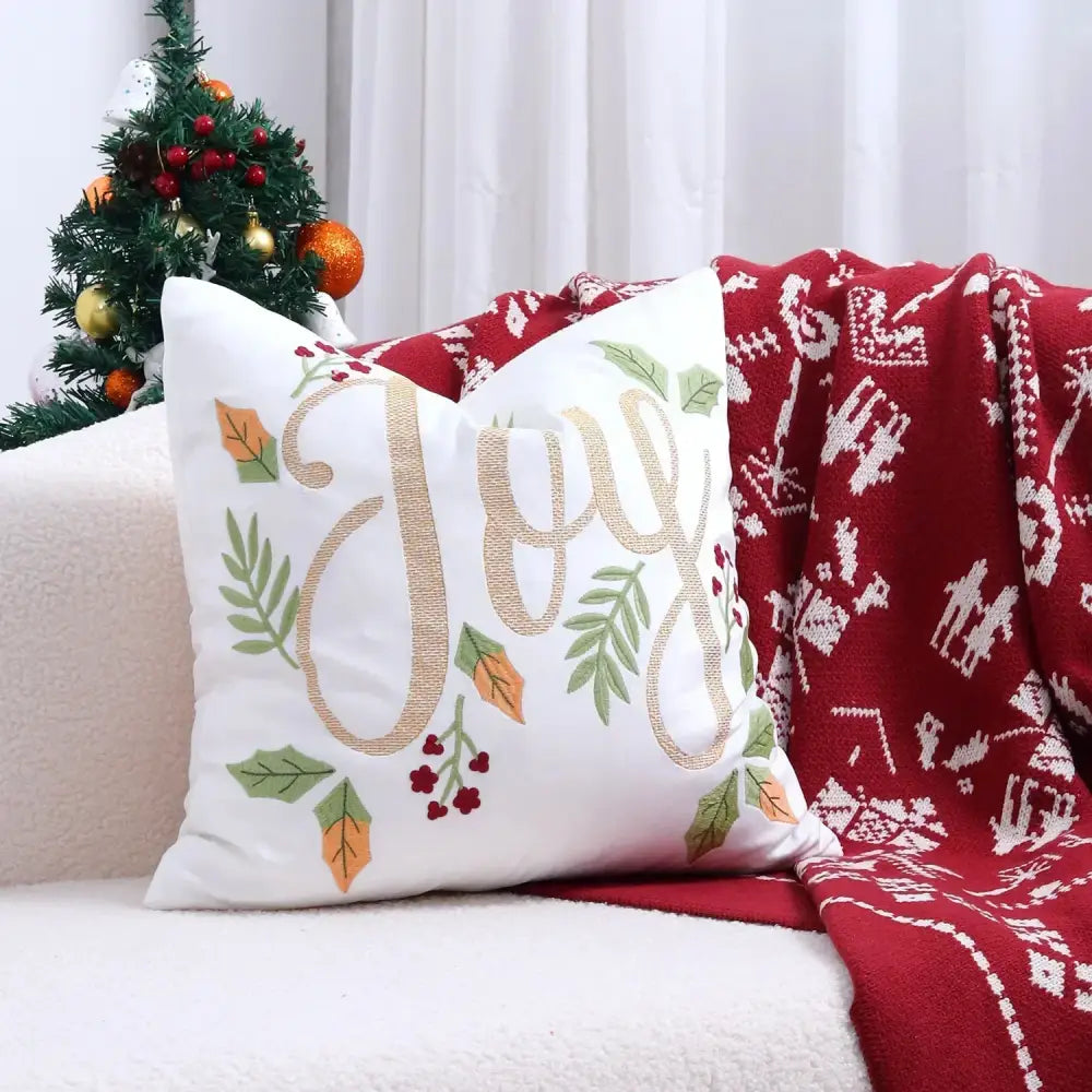 White cushion cover with gold embroidered joy and festive green and orange leaves with red berries for christmas tree decor