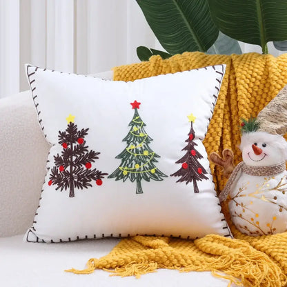 White DecorBites™ cushion cover featuring embroidered Christmas tree designs in black, green, red, and yellow stars