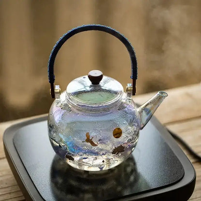 A colorful enamel glass teapot by Decorbites with blue braided handle gold accents and painted crane and lotus decor