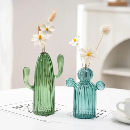 Two translucent colorful cactus glass vases in green and teal blue holding dried white daisies for home decor