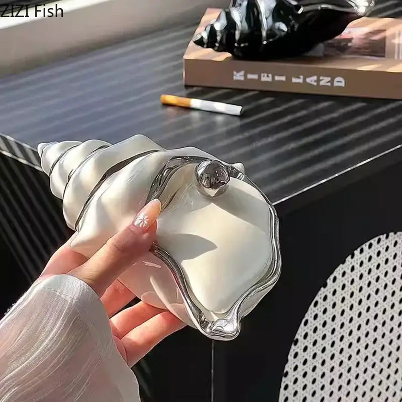A sleek white and silver ceramic decorbites conch ashtray shaped like a seashell for living room decor