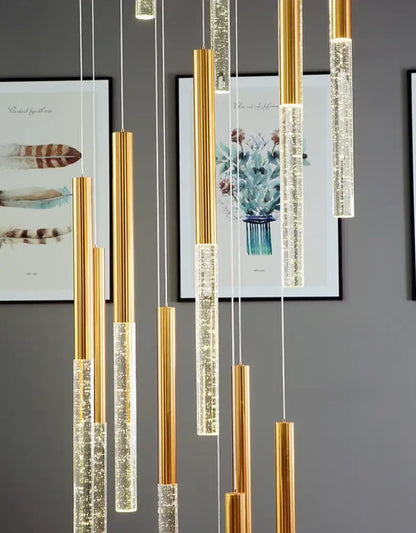Gold-toned cylindrical pendant lights with clear sparkling crystals in a contemporary crystal chandelier for large staircase