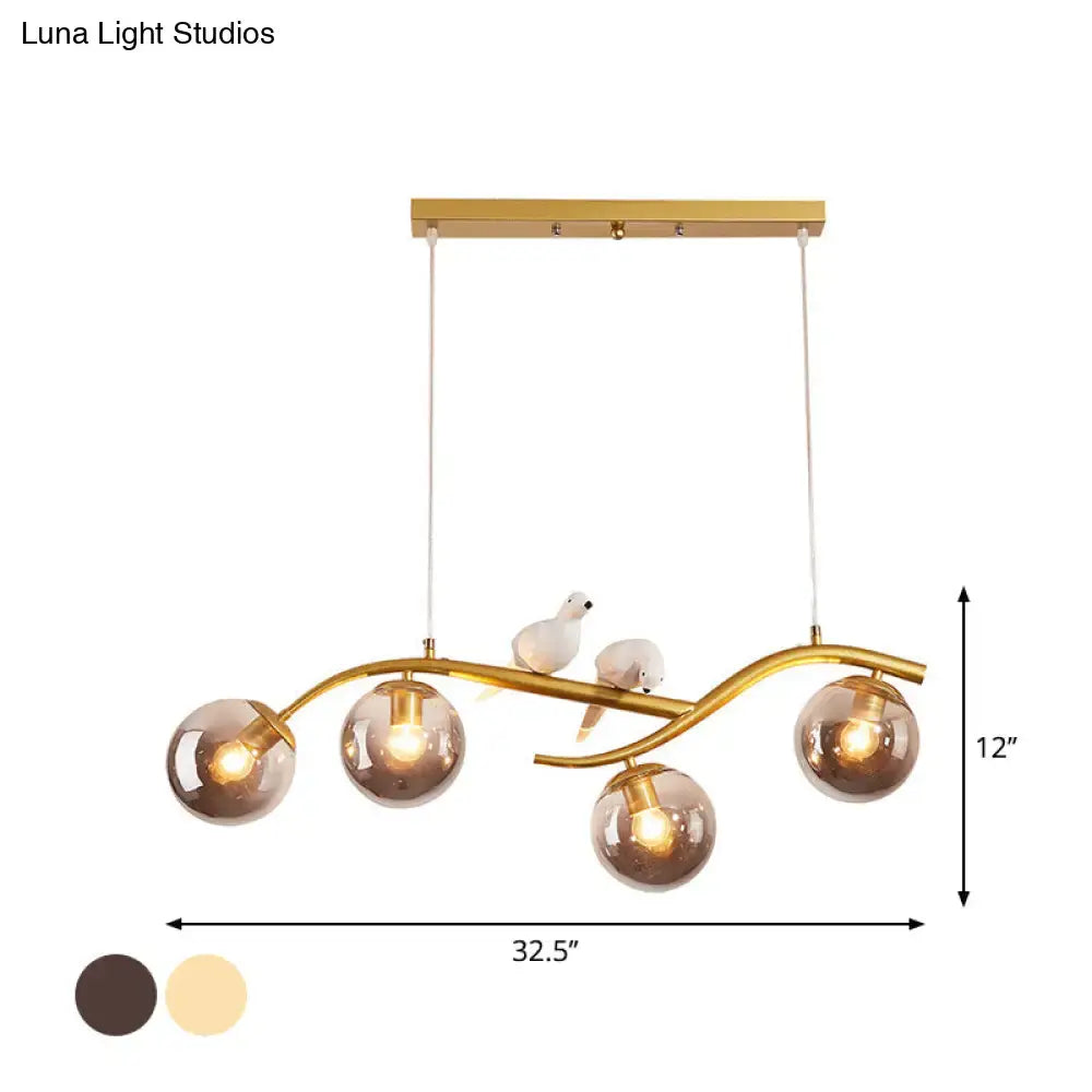 Gold-toned metal branch pendant light with four smoke grey cognac glass globes and two white ceramic bird figurines
