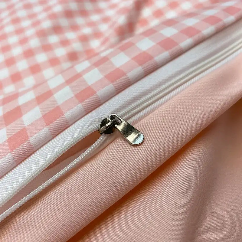 A silver-toned zipper pull on soft pink and white nordic plaid gingham fabric of decorbites 1pc duvet cover and flat sheet