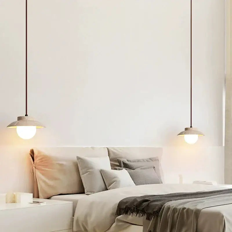 Two minimalist decorbites cream stone pendant lamps with warm bulbs and matte beige shades hang above a bed