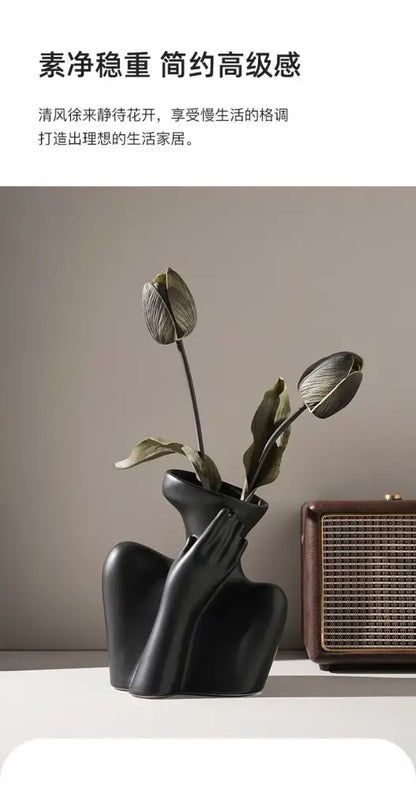 Black ceramic human vase shaped like a woman’s torso with hand cupping cheek holding dried tulips for home decor