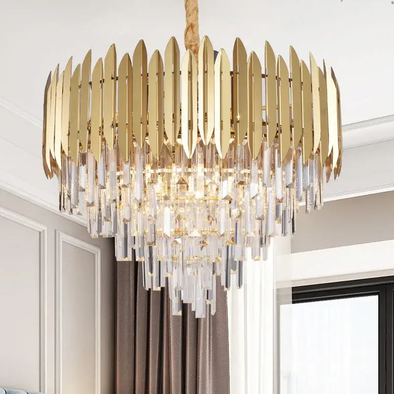 Gold-toned decorbites crystal chandelier with modern layered design featuring vertical metallic blades and clear prisms