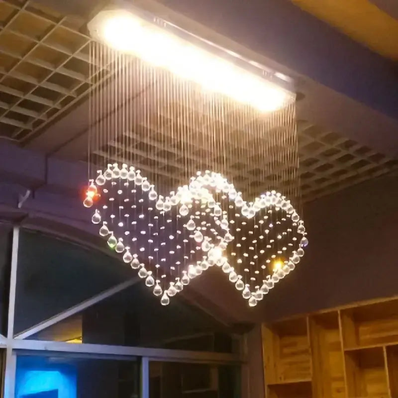 A glowing DecorBites crystal chandelier with two interlocking heart shapes made of clear crystal beads illuminated