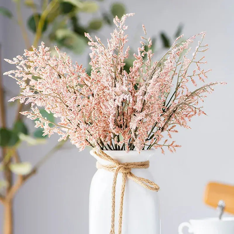 A delicate bouquet of pink dried flowers in a white ceramic vase tied with twine featuring a lemon grass branch