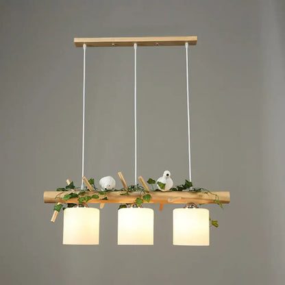 Natural wood pendant light with three cream cylindrical shades and resin bird deco among green ivy for country style restaurants