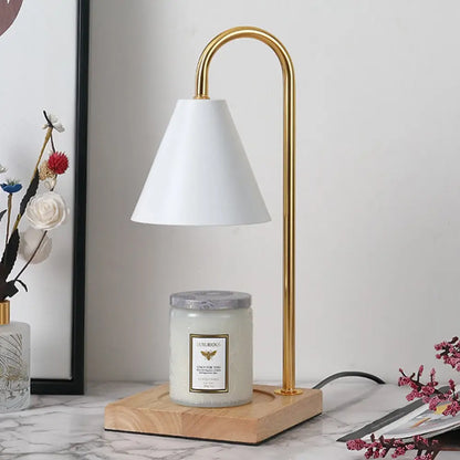 Gold-finished decorbites™ dimmable candle warmer lamp with white conical shade and wooden base warming a scented candle jar