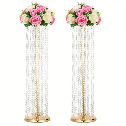 Two tall elegant metal vases with gold finish holding crystal chandeliers and pink white artificial roses for wedding decor