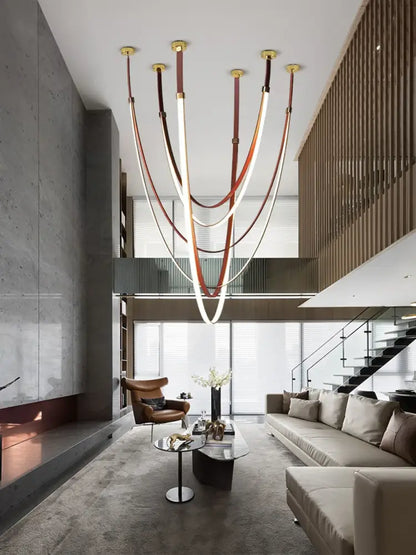 A modern LED chandelier featuring flexible leather belt straps and gold fixtures for living room decor