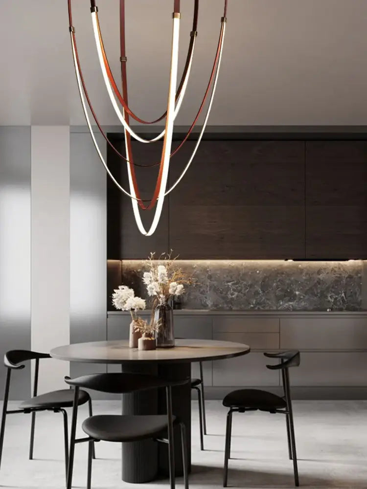 A modern DecorBites™ flexible leather belt LED chandelier with curved illuminated white and brown leather bands suspended from ceiling