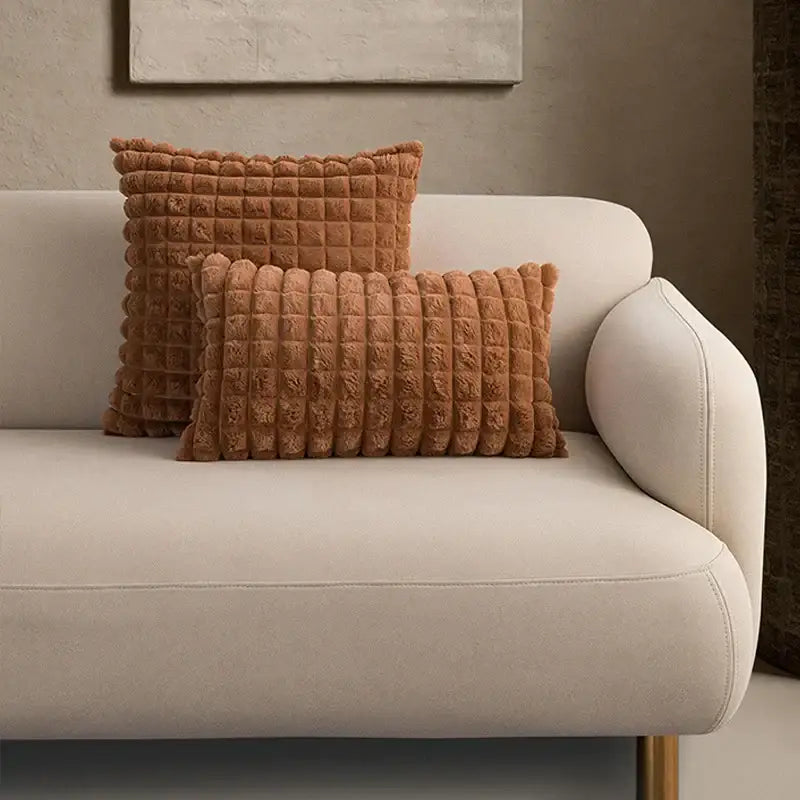 Two rust-colored decorbites fluffy faux cushion covers with quilted texture on a light beige sofa