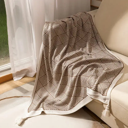 A cozy beige and cream decorbites geometric tassel blanket with tassels draped over a sofa for living room use