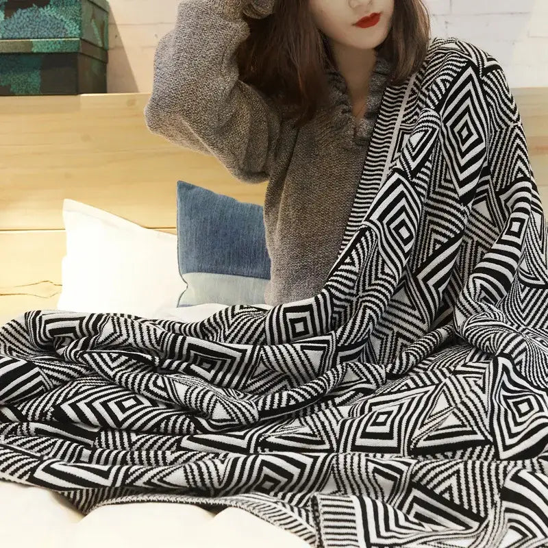 A decorbites geometric tassel black and cream knit throw blanket draped over a person’s lap in a living room setting