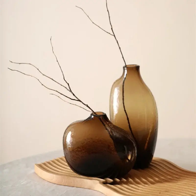Two amber glass vases with smooth rounded forms and slender necks on a wooden tray for single flower display