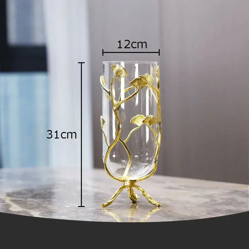 A tall clear glass vase with a golden ginkgo leaf glass frame standing on ornate legs for modern desk decoration