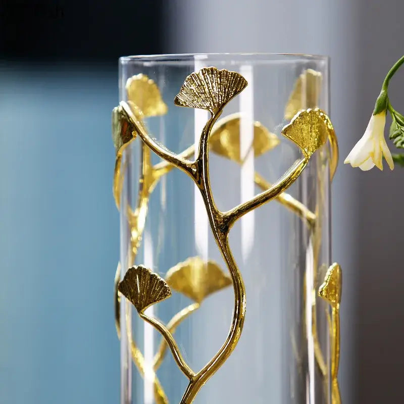 A clear glass vase with intricate gold-toned ginkgo leaf embellishments for modern desk decoration