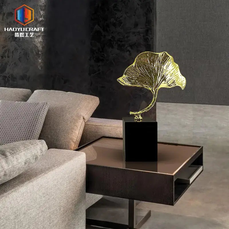Golden decorbites ginkgo leaf metal sculpture with intricate veining on sleek black base for home decor accent