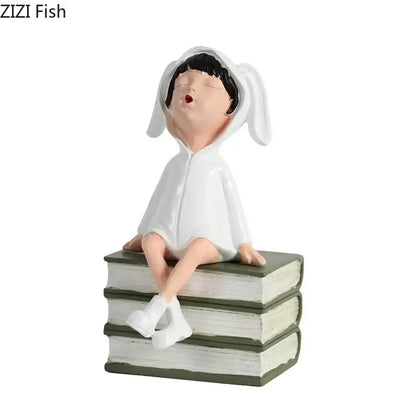 White resin sculpture figure of a child in bunny pajamas yawning on stacked books for modern decor