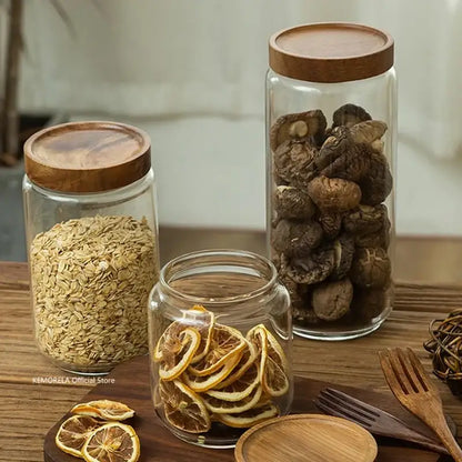 Three clear decorbites glass airtight canisters with wooden lids containing oats mushrooms and sliced citrus for kitchen storage