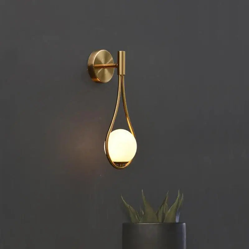 Gold-toned decorbites glass ball brass wall lamp with a sleek teardrop frame and warm-glowing LED bulb for bedroom lighting