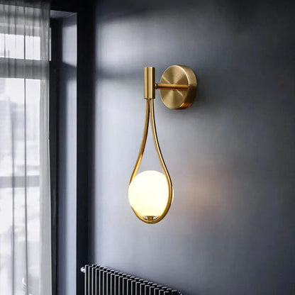 Gold-toned decorbites glass ball brass wall lamp with teardrop frame and warm-glowing LED bulb for bedroom lighting