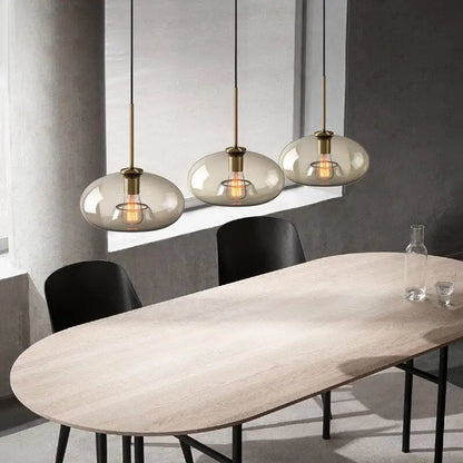 Three modern decorbites™ glass pendant lights with smoked glass globes and brass accents hanging above dining table