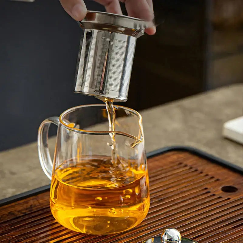 Silver stainless steel tea infuser poured into clear glass teapot with golden liquid in decorbites™ tea jug set