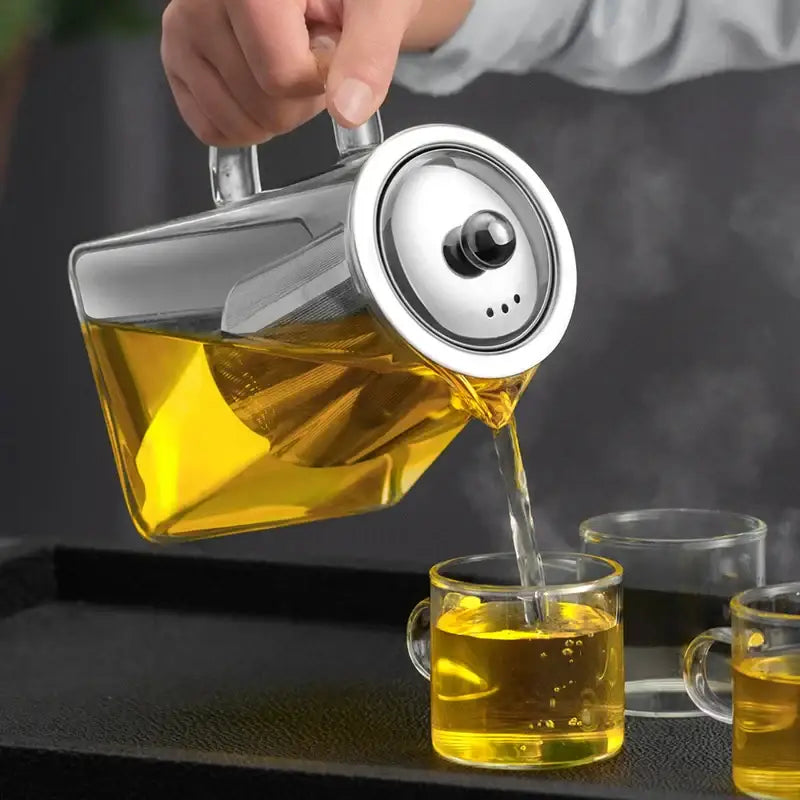 A sleek decorbites glass tea pot with stainless steel lid pours golden tea into matching clear glass cups