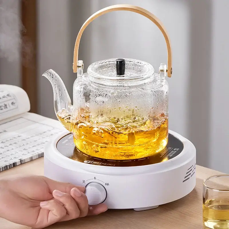 Clear decorbites glass tea pot with bamboo handle black lid on white electric heating base for brewing tea