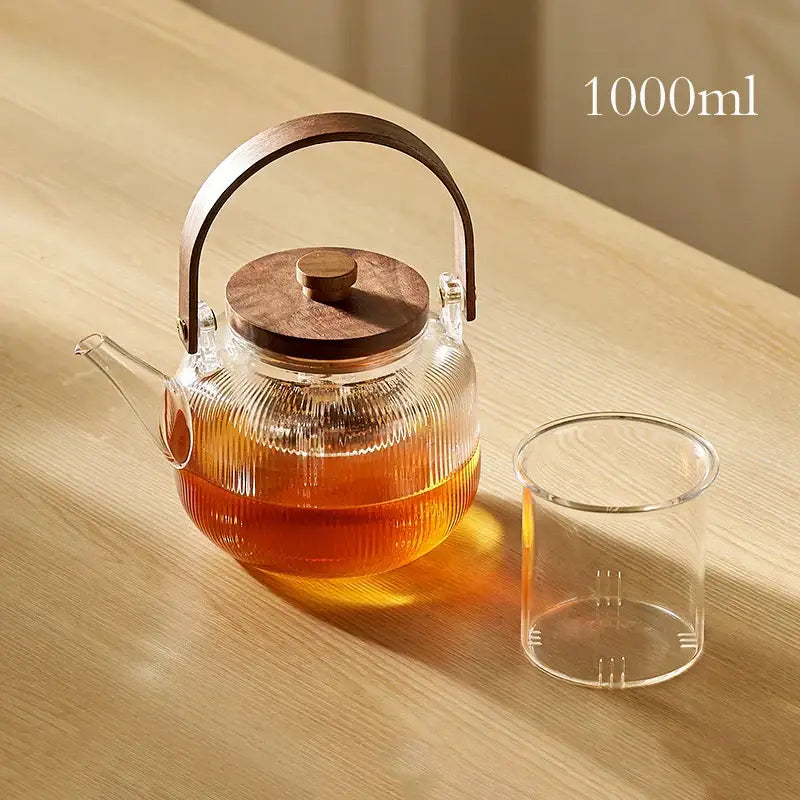 A 1000ml decorbites glass tea pot with wooden handle and lid filled with amber tea and stainless steel filter