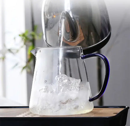 A clear glass teapot with a sleek blue handle is being filled with hot water from a stainless steel kettle decorbites glass teapot