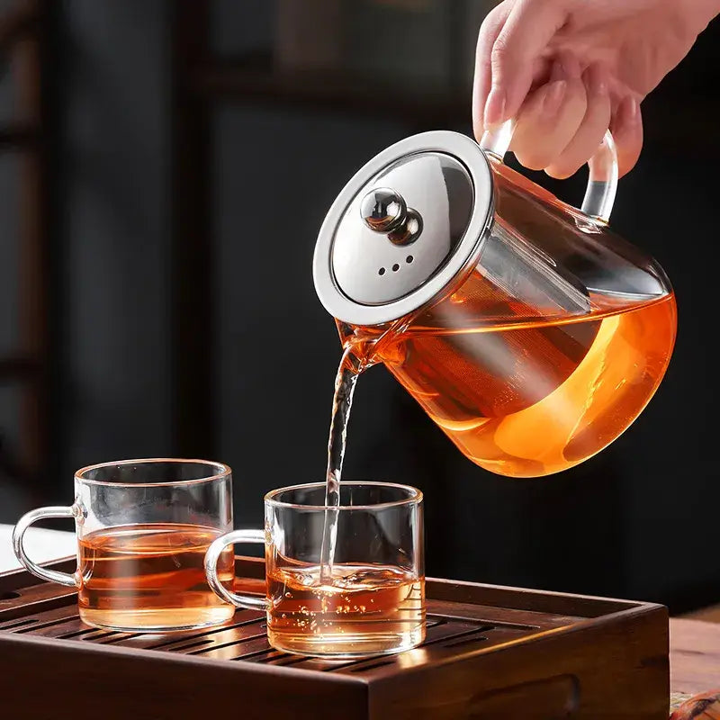 Clear glass decorbites glass teapot with silver lid pouring amber tea into matching cups for puer tea and coffee