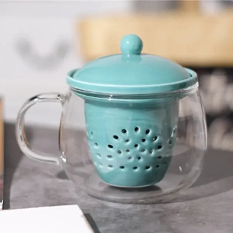 A turquoise ceramic filter with lid inside a clear glass mug from the decorbites glass teapot set for puer tea infusion