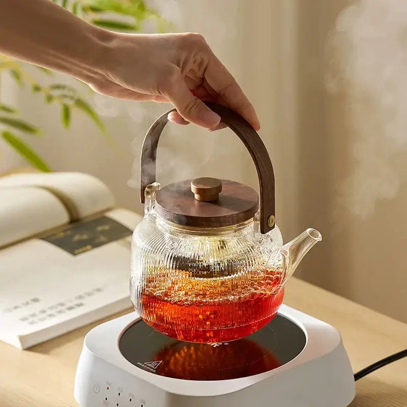 DecorBites glass teapot set features a clear glass teapot with wooden handle and lid filled with steaming red tea