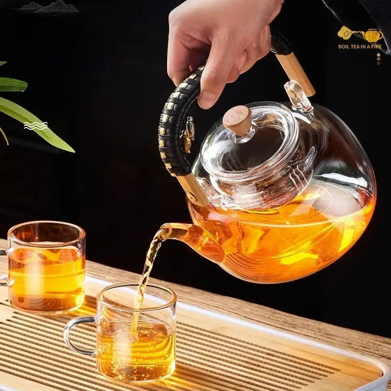 Clear glass decorbites glass teapot with wooden lid and black handle pouring amber tea into matching glasses