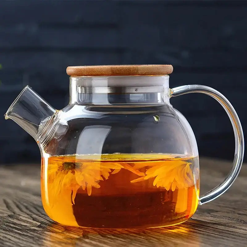 Clear glass decorbites glass teapot with bamboo lid and infuser for tea brewing filled with golden tea and floating flowers
