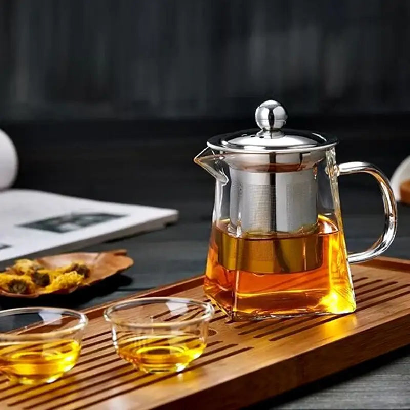 Decorbites™ glass teapot with stainless steel infuser and lid filled with amber tea featuring a steel infuser